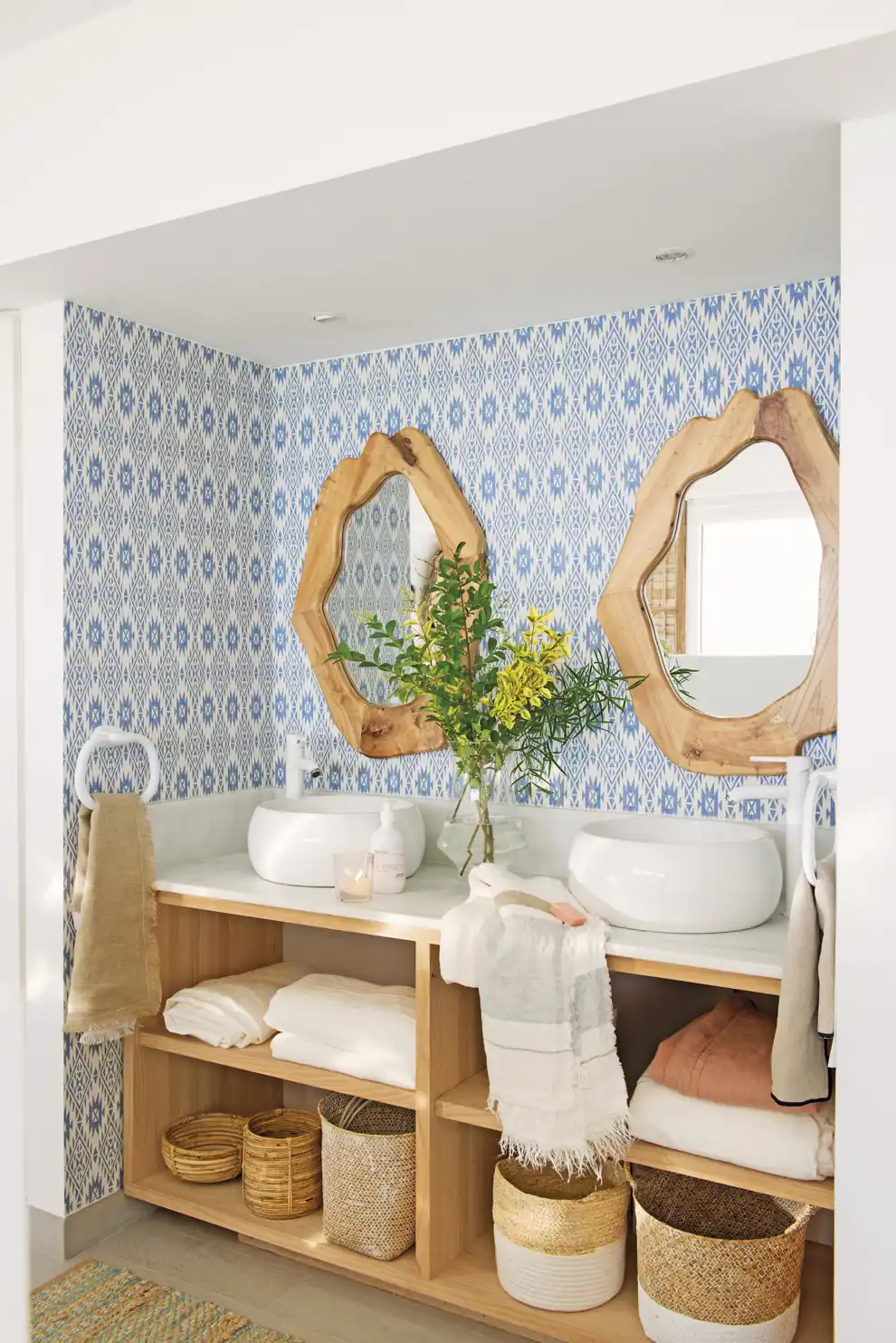 00527599 Cuarto de baño con doble lavabo, pared con motivos azules y un mueble abierto con toallas y cestas de almacenaje