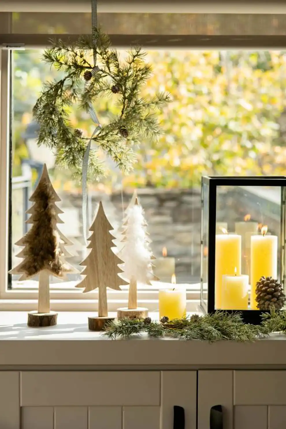 Ventana navideña decorada con una corona de Navidad, velas y mii arbolitos de madera