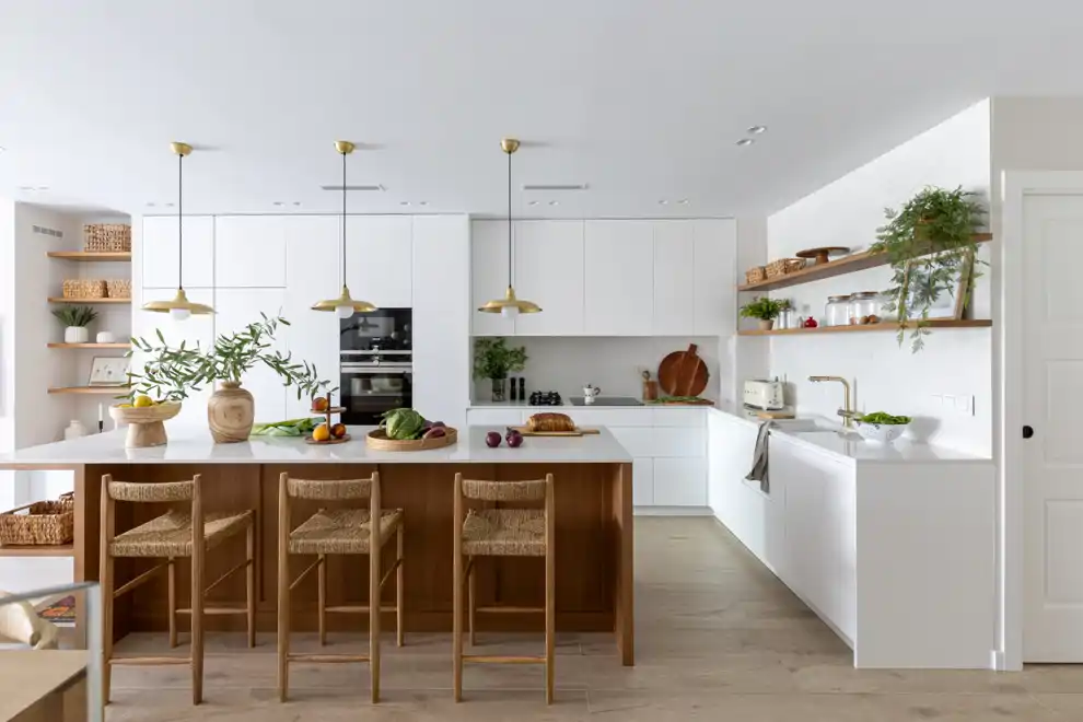 La cocina, con su gran isla de madera, sus muebles blancos lacados, sus encimeras de silestone y sus detalles en oro cepillado se ha convertido en el corazón del hogar